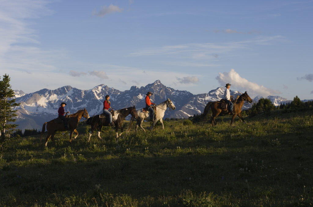 Horseback riding in the Chilcotin region, British Columbia, with mountain views and grassy field.